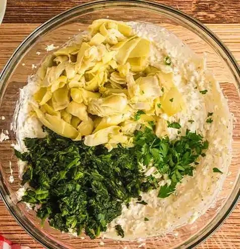 hot-spinach-artichoke-dip-preparation-steps11 Homemade creamy spinach artichoke dip mixture in a glass bowl ready for baking