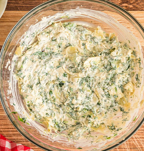 hot-spinach-artichoke-dip-preparation-steps12 Homemade creamy spinach artichoke dip mixture in a glass bowl ready for baking